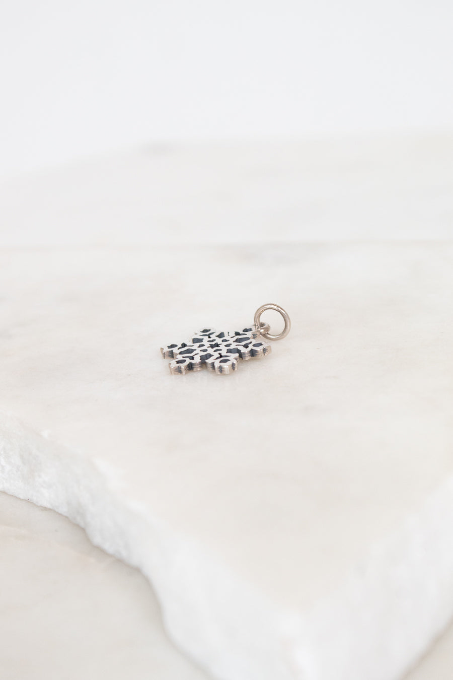 Silver charm with a snowflake design on a white background