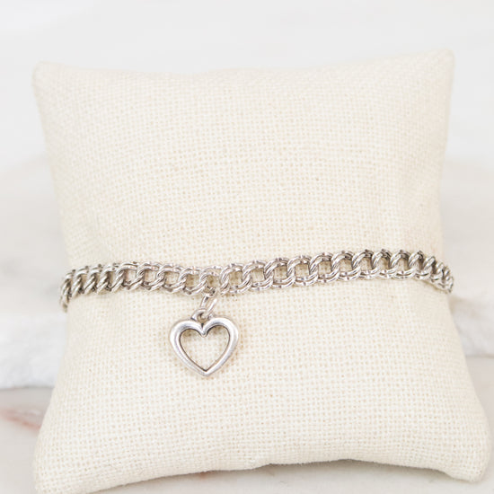 Silver bracelet with a heart charm on a white cushion
