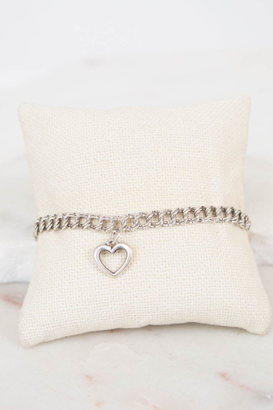Silver bracelet with a heart charm on a white cushion