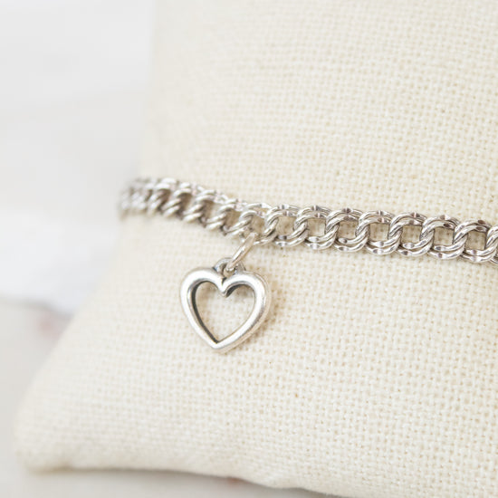 Silver bracelet with a heart charm on a white cushion