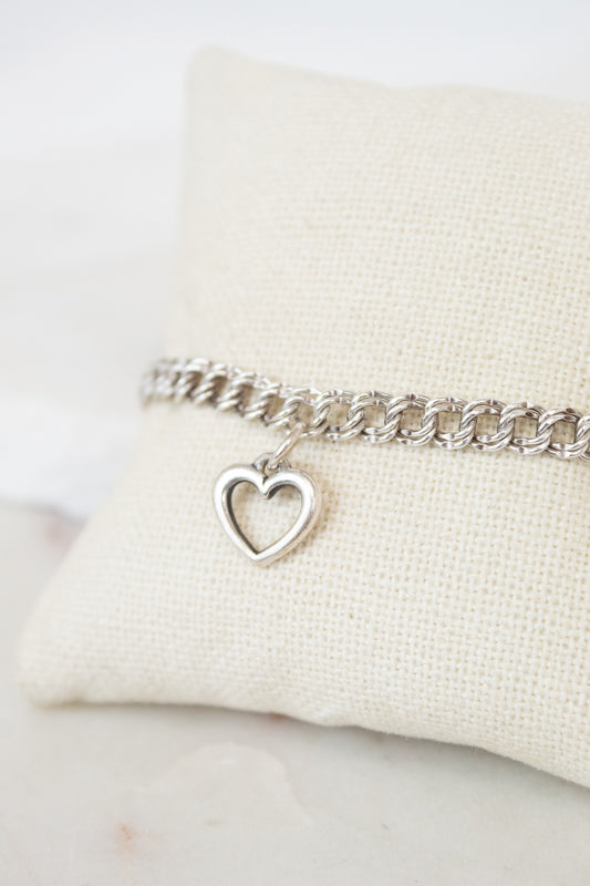 Silver bracelet with a heart charm on a white cushion