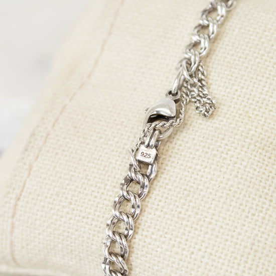Silver chain bracelet on a beige cushion with a white background