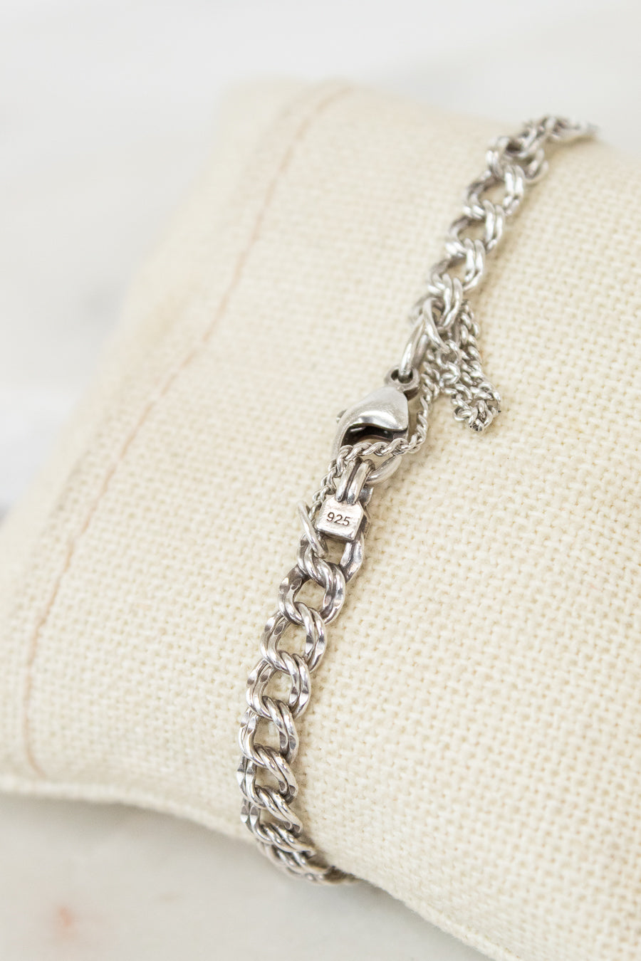 Silver chain bracelet on a beige cushion with a white background