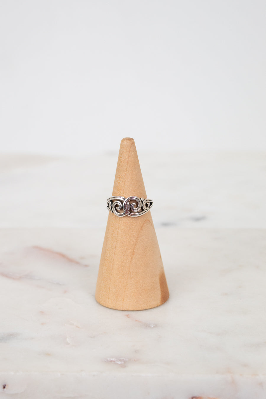 Silver ring on a wooden cone against a marble background