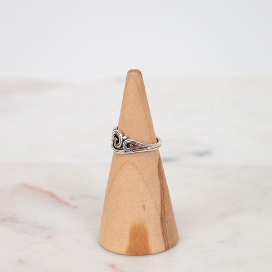 Silver ring on a wooden cone against a white background