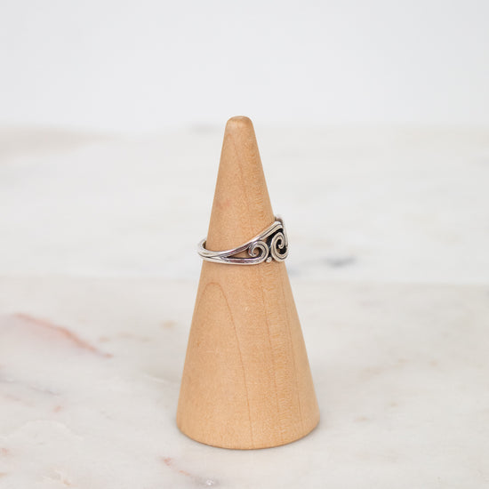Silver ring on a wooden cone against a white background