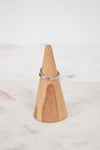Wooden cone-shaped ring holder with a silver ring on a marble surface