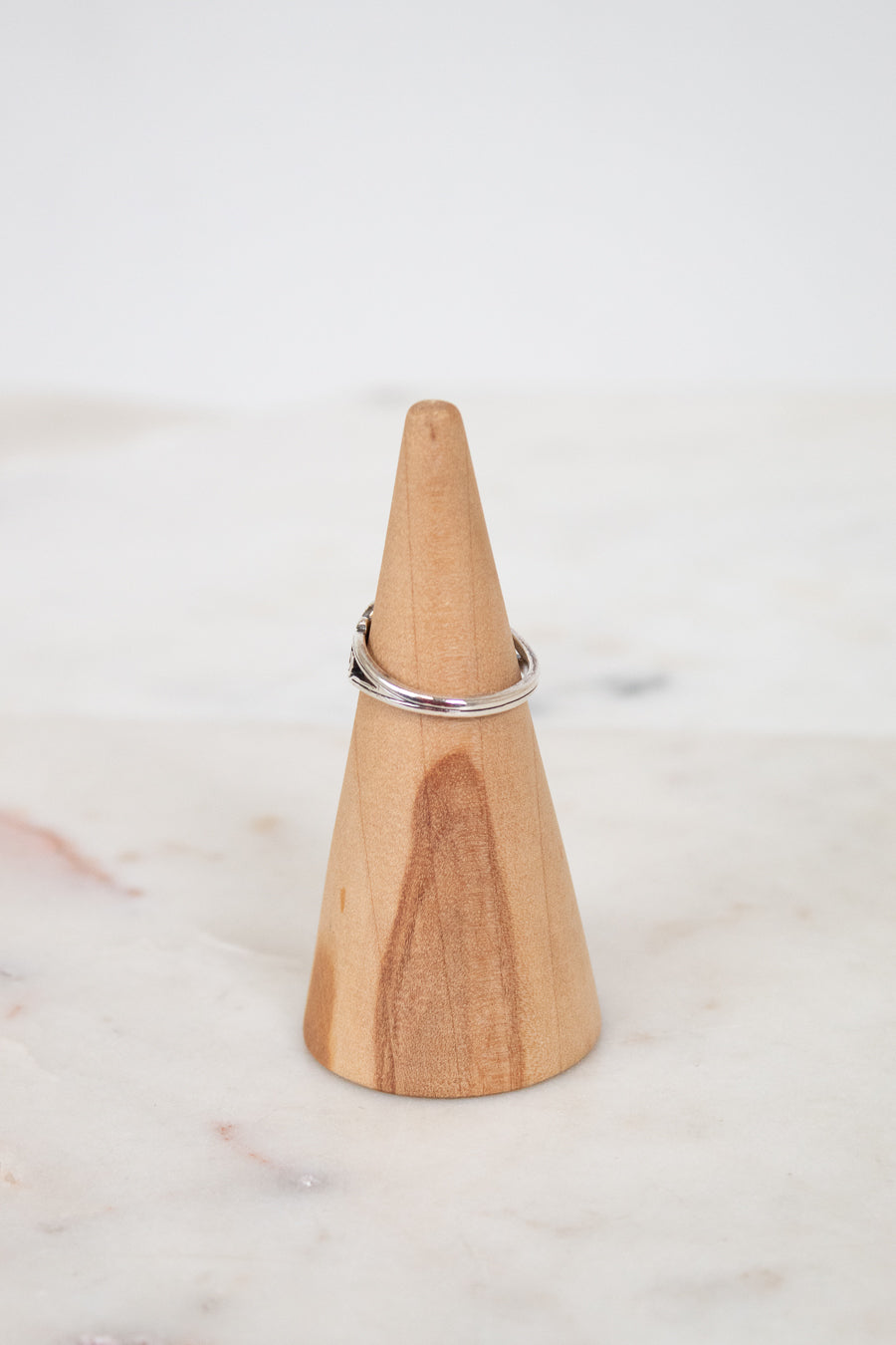 Wooden cone-shaped ring holder with a silver ring on a marble surface