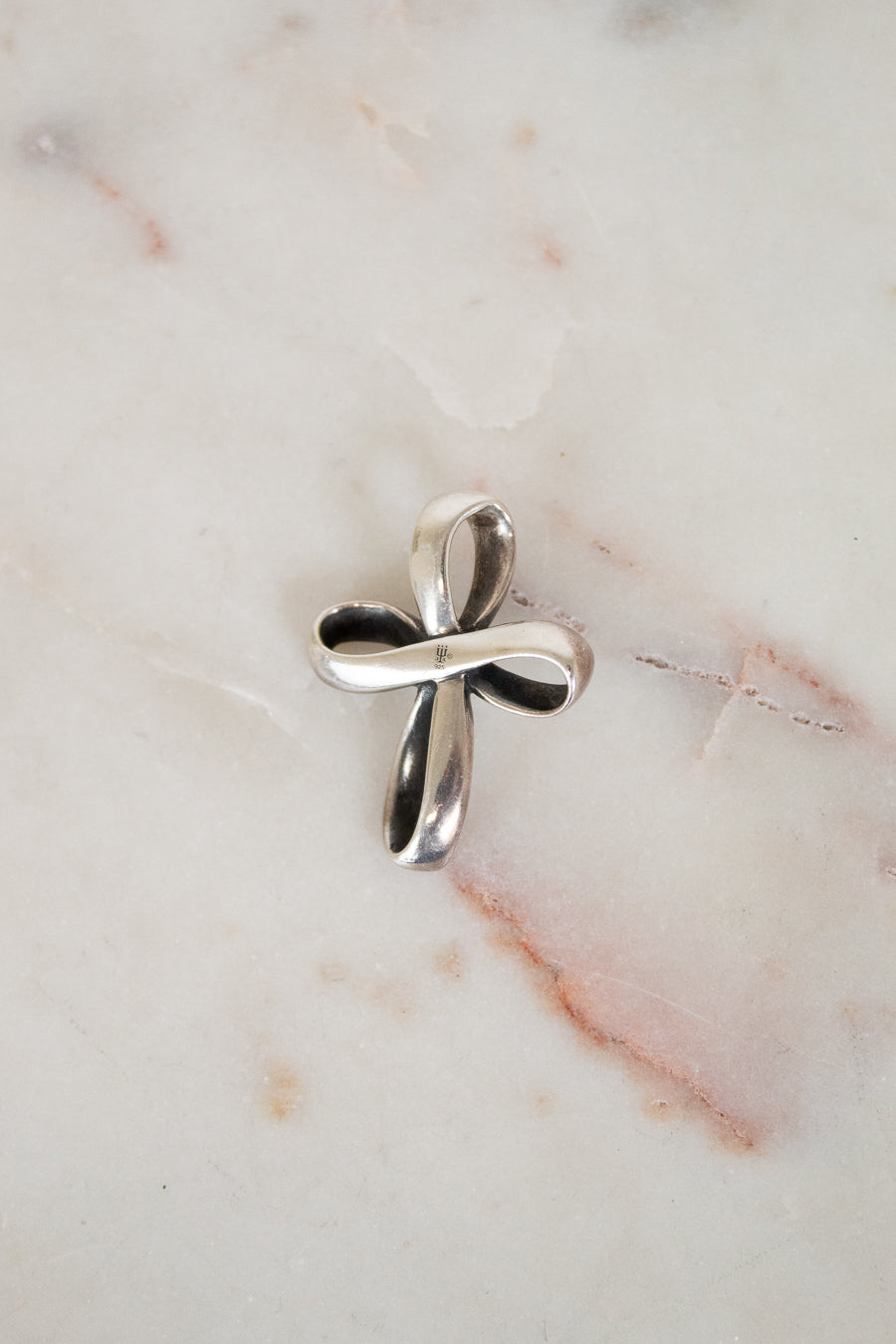 Silver cross pendant on a marble surface