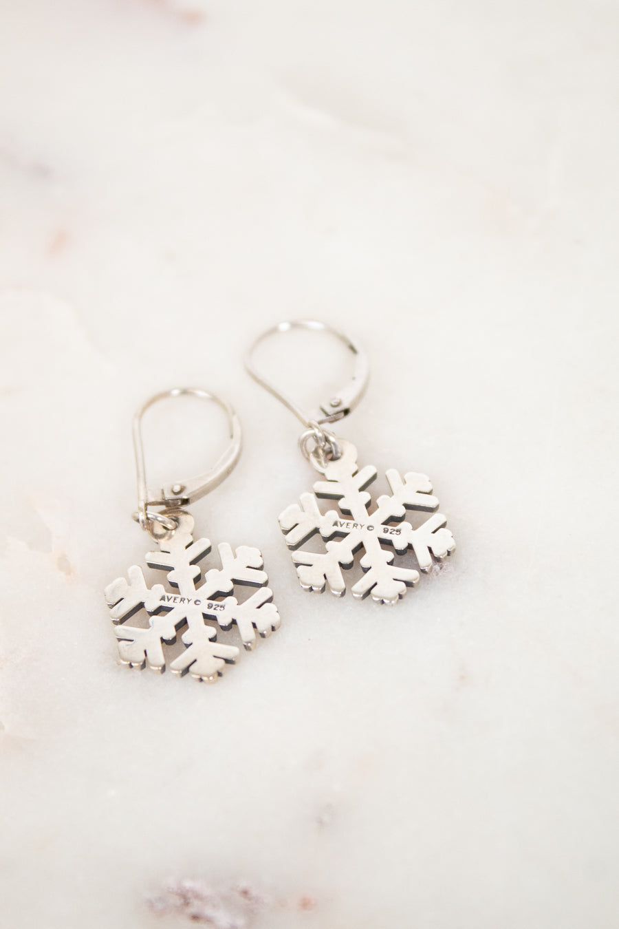 Silver snowflake earrings on a light marble background