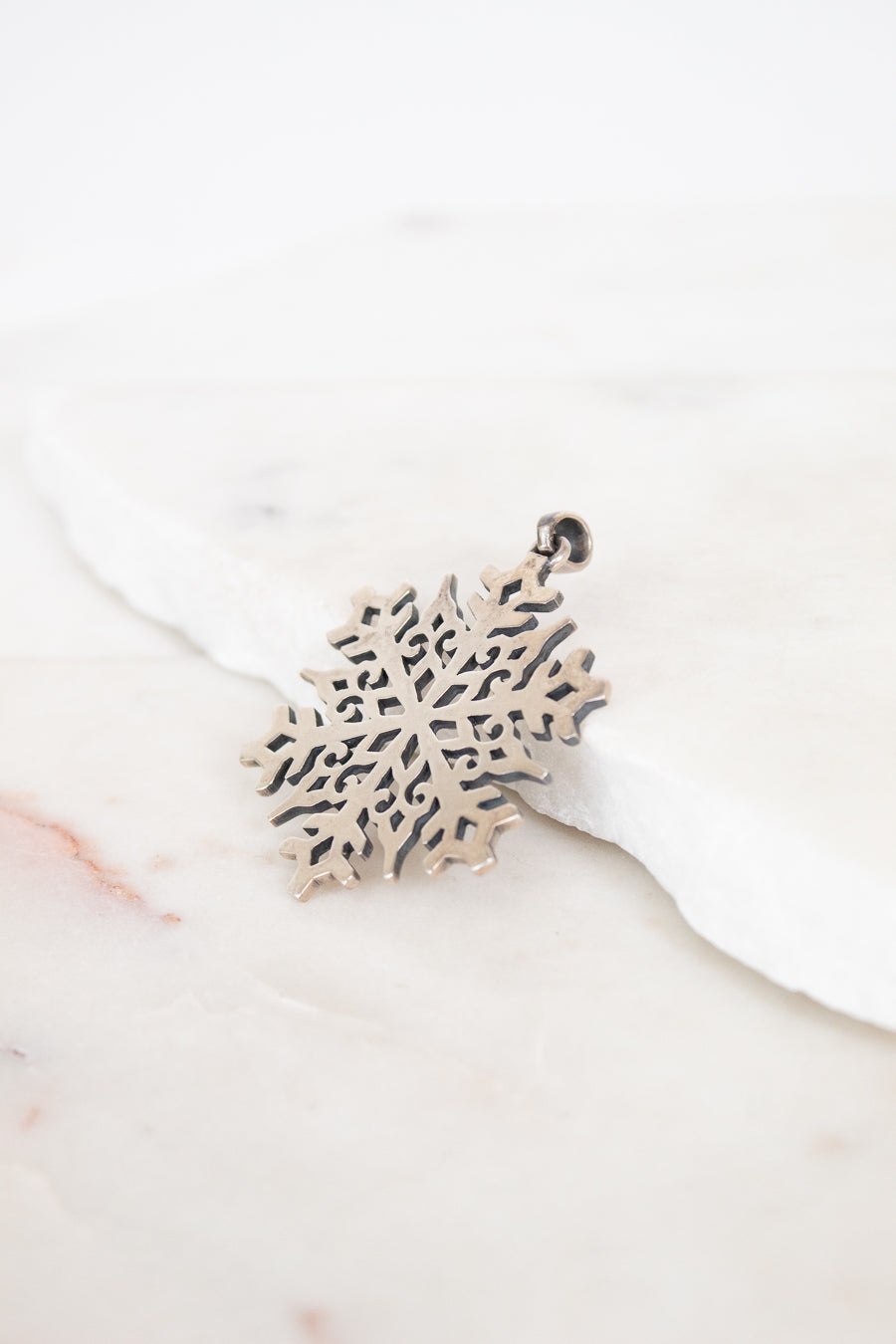 Silver snowflake-shaped pendant on a white background
