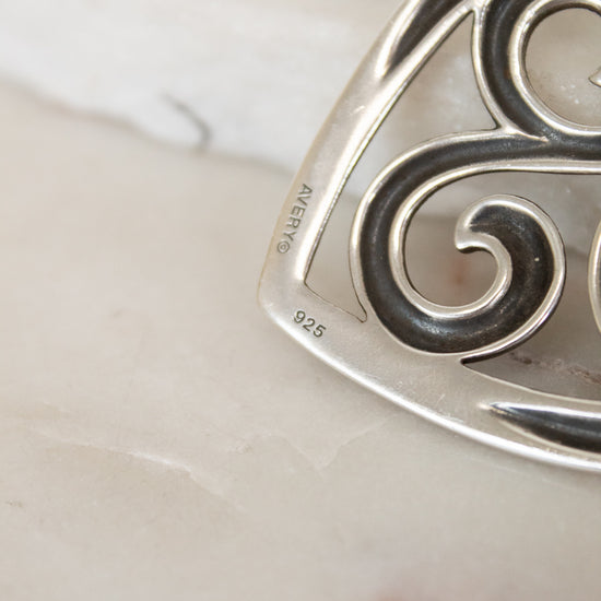 Silver pendant with intricate design on a marble surface