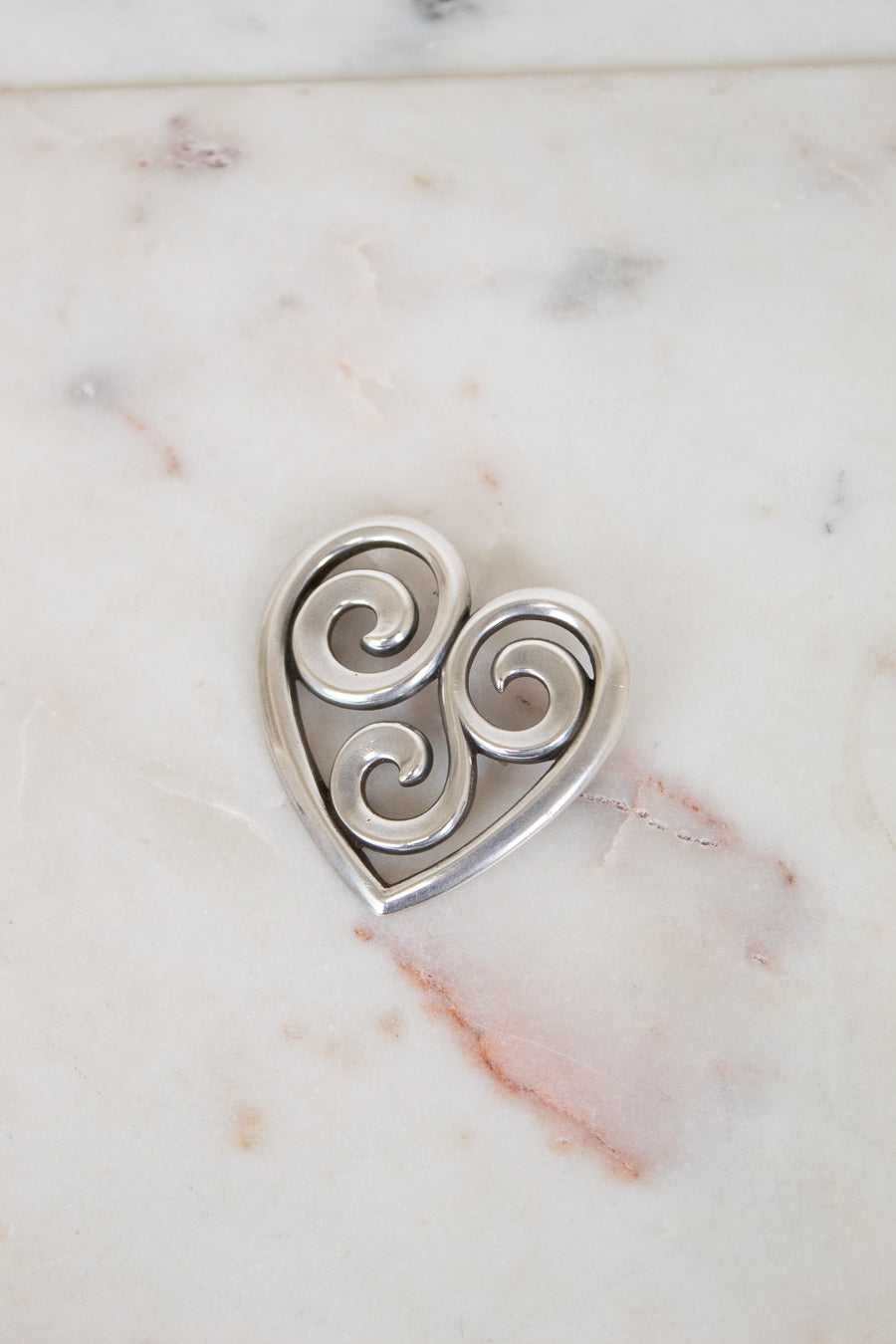 Silver heart-shaped pendant with swirling designs on a marble surface