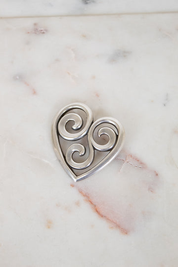 Silver heart-shaped pendant with swirling designs on a marble surface