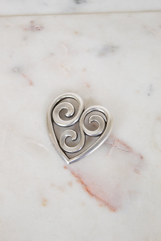 Silver heart-shaped pendant with swirling designs on a marble surface