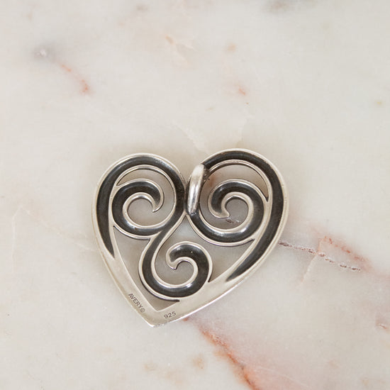 Silver heart-shaped pendant with swirling design on a marble surface