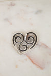 Silver heart-shaped pendant with swirling design on a marble surface