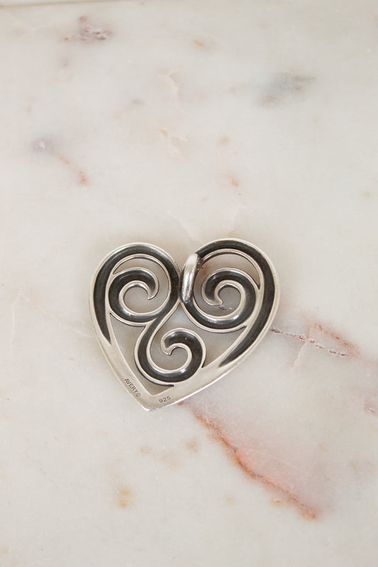 Silver heart-shaped pendant with swirling design on a marble surface