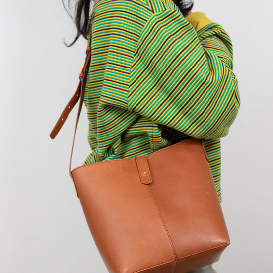 Person wearing a green and yellow striped sweater with a brown leather bag on a white background