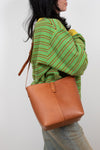 Person wearing a green and yellow striped sweater with a brown leather bag on a white background