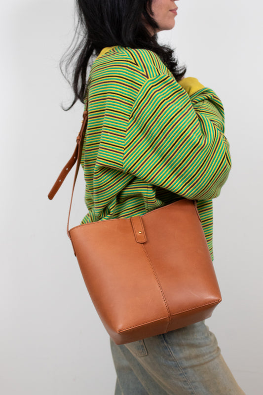 Person wearing a green and yellow striped sweater with a brown leather bag on a white background