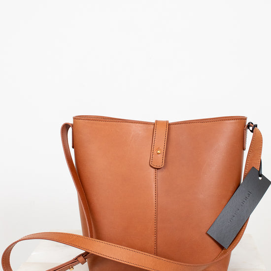 Brown leather handbag with a tag on a light wooden surface