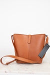 Brown leather handbag with a tag on a light wooden surface
