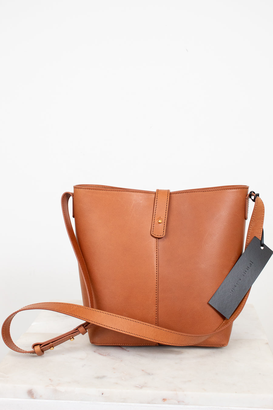 Brown leather handbag with a tag on a light wooden surface