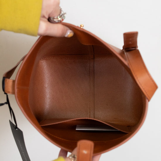 Brown leather handbag held by a person wearing a yellow sleeve.