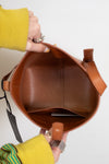 Brown leather handbag held by a person wearing a yellow sleeve.