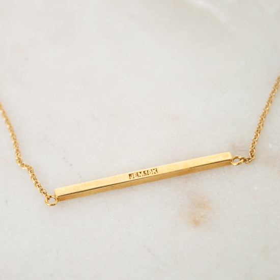 Gold necklace with a bar pendant on a light background