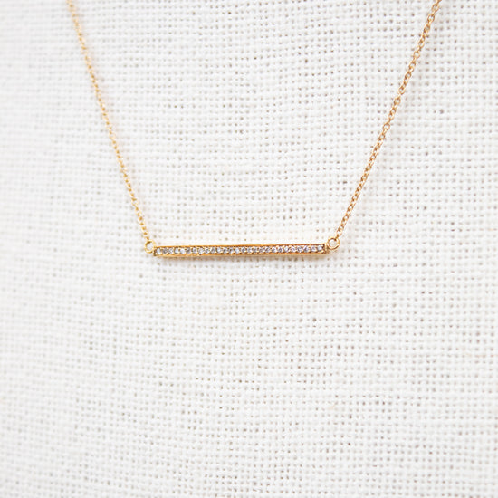 Gold necklace with a bar pendant on a light gray textured background