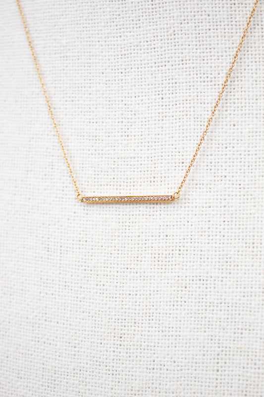 Gold necklace with a bar pendant on a light gray textured background