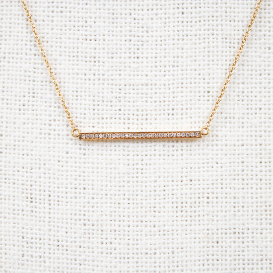 Gold necklace with a bar pendant on a light gray background