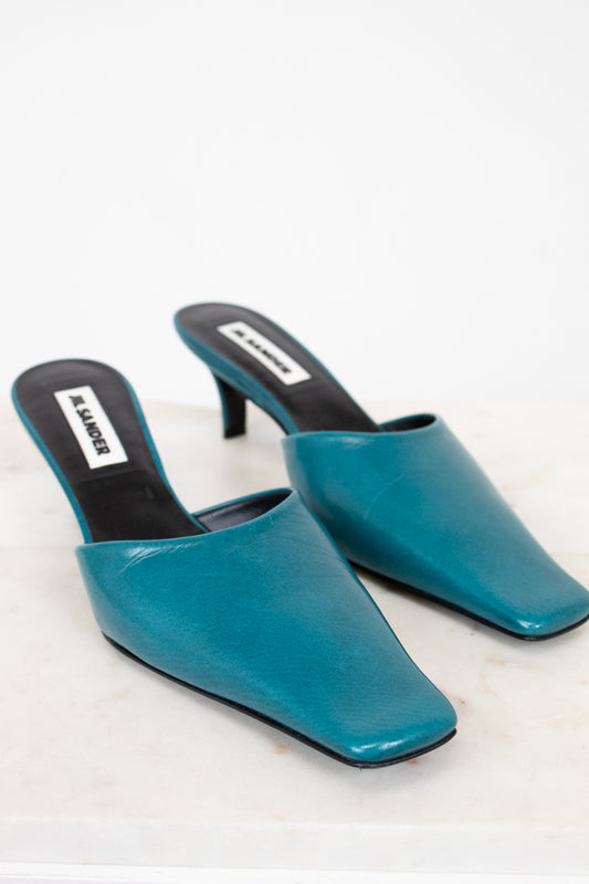 Pair of teal high-heeled mules on a white background