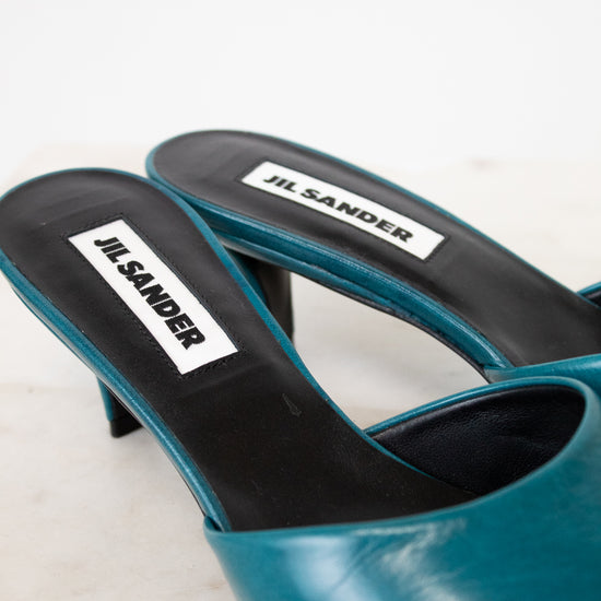 Teal high-heeled shoe with black sole on a white background