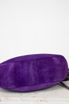 Purple suede bag on a light gray surface with a white background