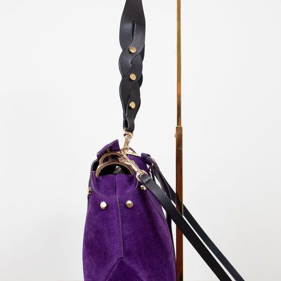 Purple handbag with a black strap on a white background