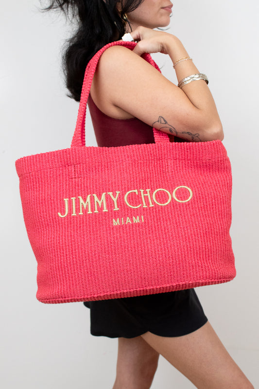 Person holding a pink tote bag with 'Jimmy Choo Miami' branding.