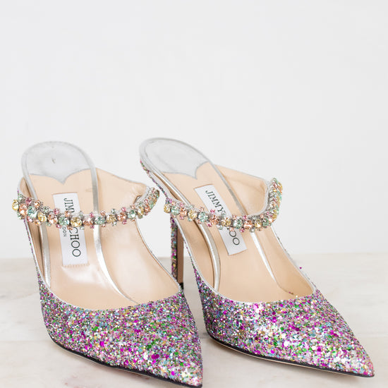 Pair of glittery high-heeled shoes with embellished straps on a light background