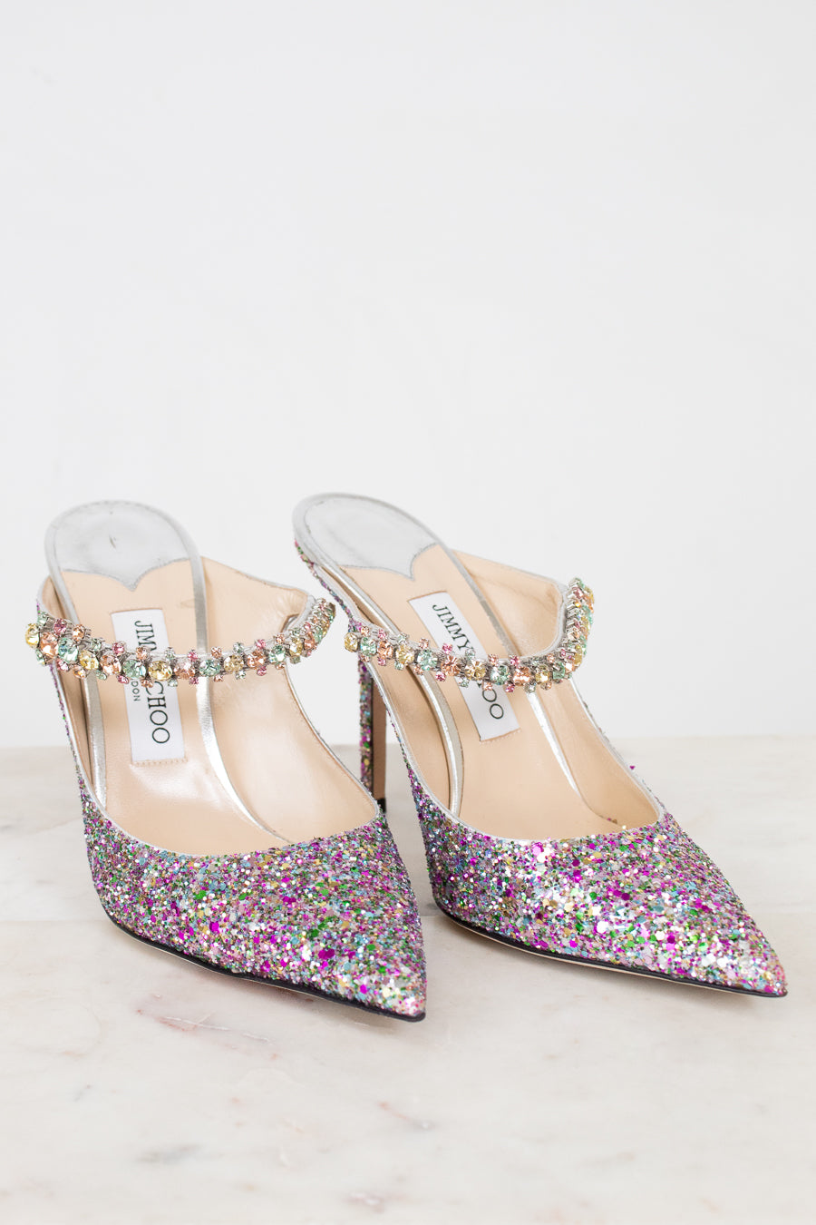 Pair of glittery high-heeled shoes with embellished straps on a light background