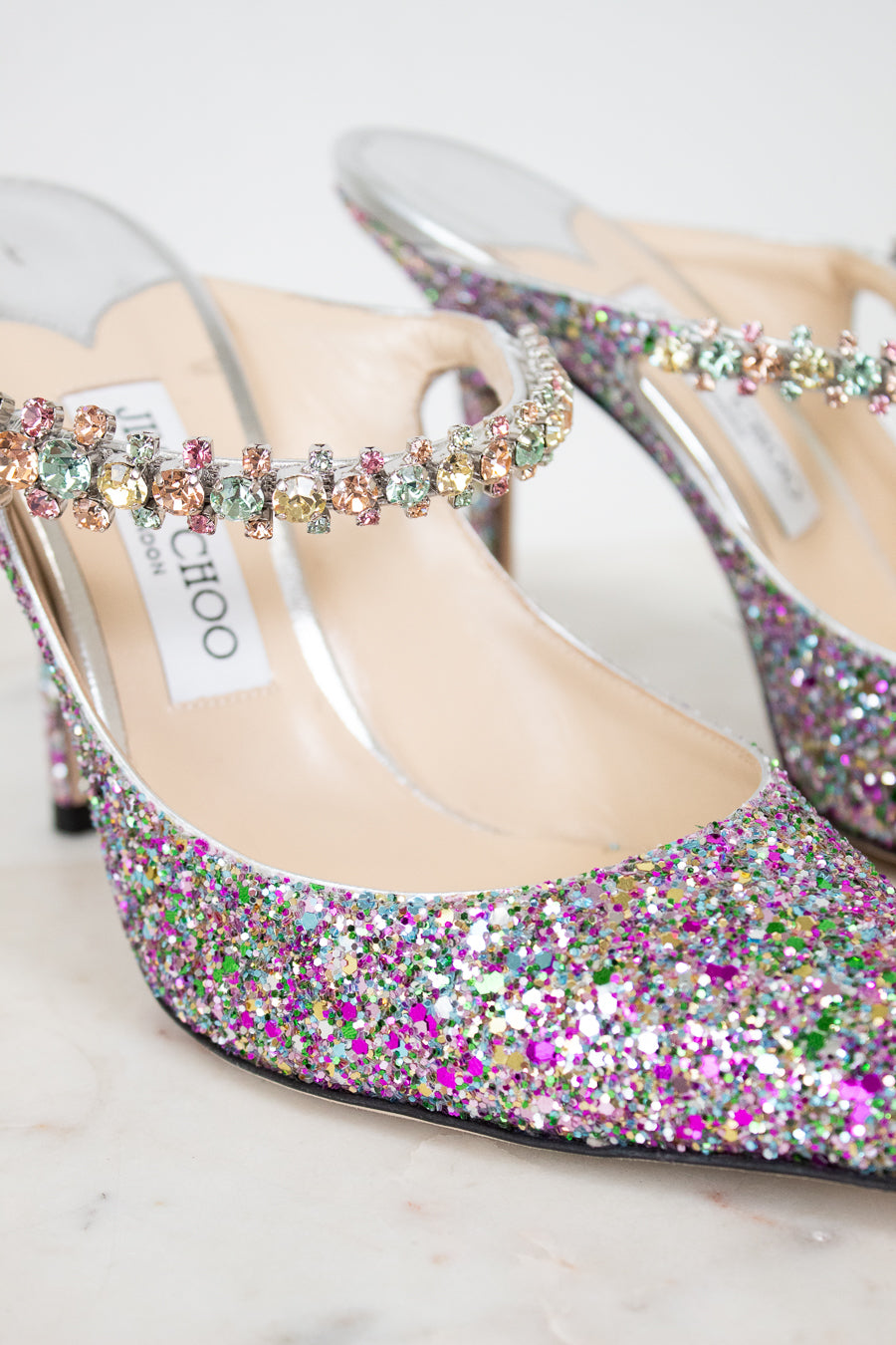 Multicolored glittery high-heeled shoes with 'Jimmy Choo' label on a light background