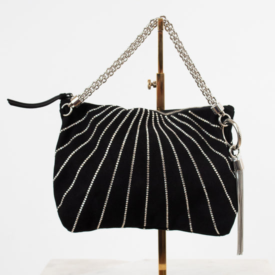 A black suede shoulder bag with silver beaded vertical stripes and a silver chain strap, displayed on a gold stand against a white background.
