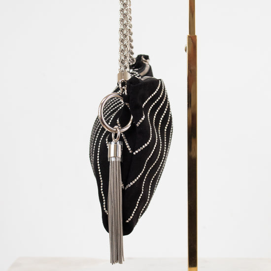 A black velvet evening clutch bag with silver rhinestone wave detailing, a silver chain strap, and a silver tassel keychain, displayed on a gold metal stand against a white background.
