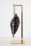 A black velvet evening clutch bag with silver rhinestone wave detailing, a silver chain strap, and a silver tassel keychain, displayed on a gold metal stand against a white background.