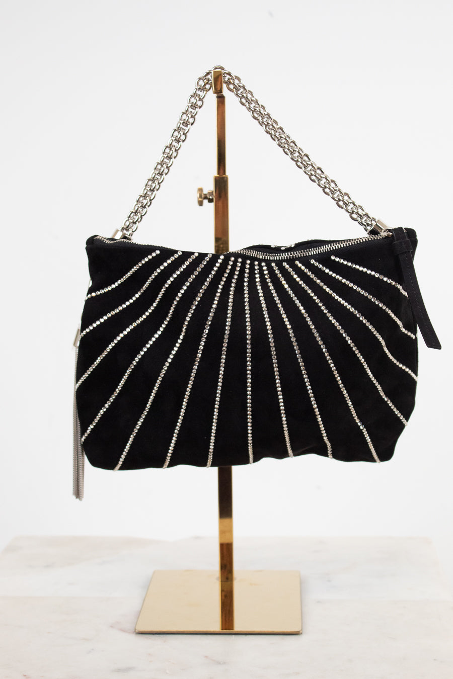 A black velvet shoulder bag with vertical silver rhinestone stripes, displayed on a gold metal stand against a white background.