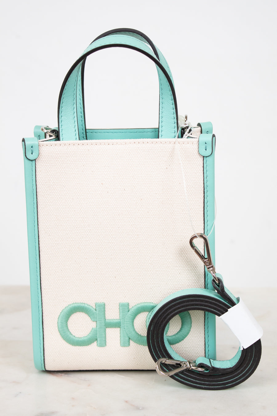 A structured mini tote bag with a cream canvas body and mint green trim, featuring a large 'CHOO' logo on the front and a detachable black and mint green shoulder strap.