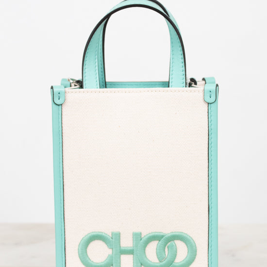 A structured mini tote bag with a cream-colored front panel and mint green trim, handles, and logo lettering, displayed on a light marble surface against a white background.