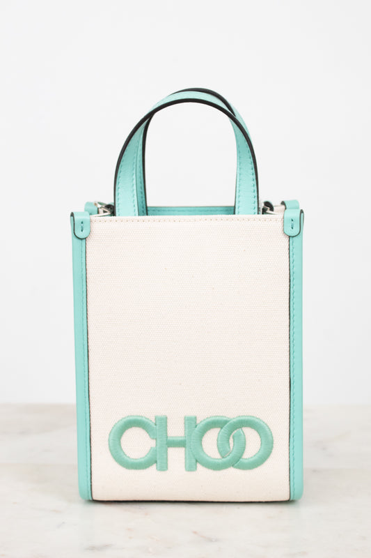 A structured mini tote bag with a cream-colored front panel and mint green trim, handles, and logo lettering, displayed on a light marble surface against a white background.