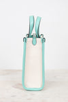 A structured mini tote bag with a cream canvas body and mint green leather trim and handles, standing upright on a light marble surface against a white background.
